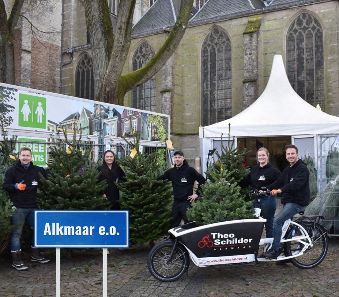 Het team met kerstbomen en de bakfiets van Theo Schilder Tweewielers naast de Grote Sint Laurenskerk